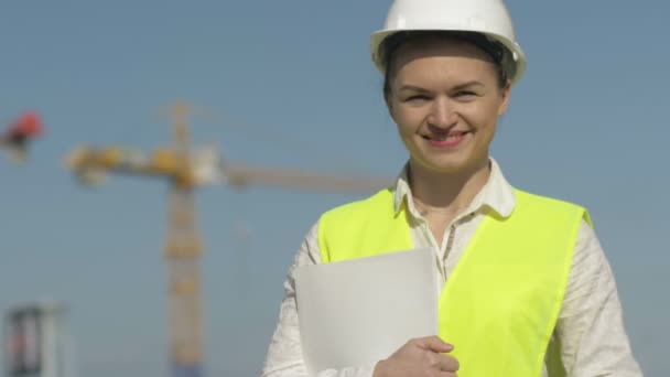 Flickbyggare i skyddskläder på byggarbetsplatsen. Flicka håller en mapp med dokument och leenden. — Stockvideo