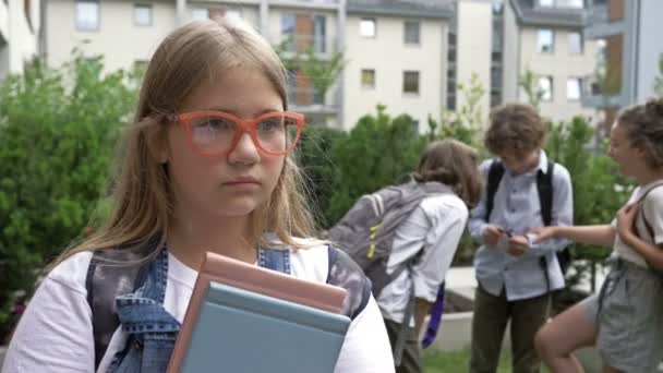 Porträt einer traurigen Schülerin. Eine Gruppe von Schulkindern verspottet das Mädchen. Kindliche Grausamkeit. Mobbing in der Schule. — Stockvideo