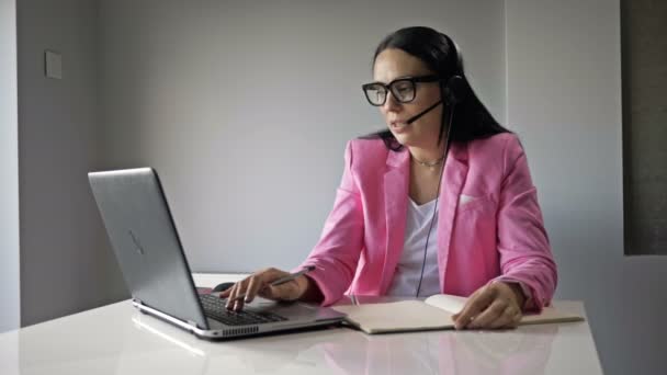 Una mujer atractiva trabaja en la computadora de la oficina. Ella se comunica amistosamente con el cliente y escribe algo. — Vídeos de Stock