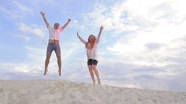 Couple joyeux saute sur le sommet d'une colline sablonneuse. Les vêtements et les visages sont teints avec de la poudre Holi. Dans le contexte du ciel. — Video