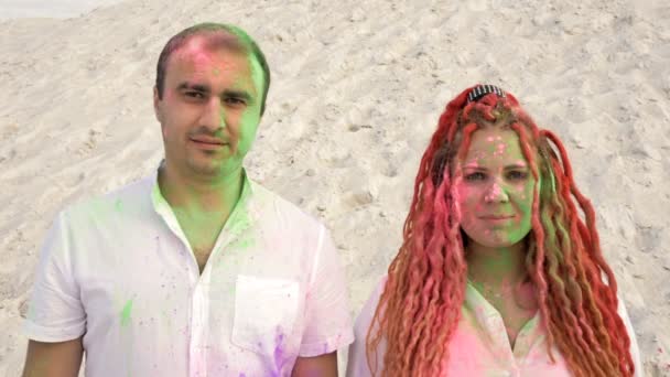 Портрет веселой молодой пары. Лица и одежда окрашены разноцветным порошком. Холи. — стоковое видео