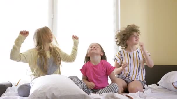 Dua pacar remaja dan seorang gadis kecil duduk di tempat tidur dan memutar kepala mereka untuk mengalahkan musik. — Stok Video