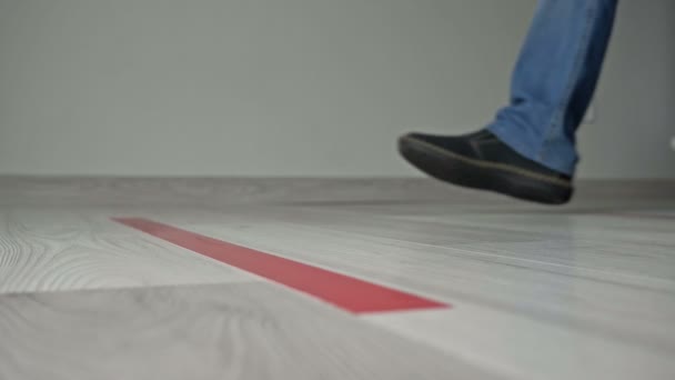 Κοντινό πλάνο των μεμονωμένων παπουτσιών και ποδιών δύο ατόμων κοντά σε μια κόκκινη λωρίδα στο πάτωμα, περιμένοντας και κρατώντας απόσταση, ενώ στέκεται στη γραμμή. Κατά τη διάρκεια του covid-19. — Αρχείο Βίντεο