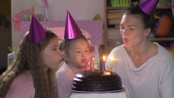Щаслива маленька дівчинка святкує свій день народження зі своєю сім'єю, її мати і сестра-підліток допомагають підірвати свічки — стокове відео