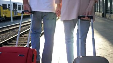 Bavulları olan yaşlı evli bir çift platform boyunca el ele yürür. Arka plan.