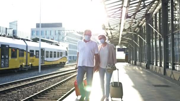Una pareja de ancianos casados con maletas camina de la mano a lo largo de la plataforma. Hay máscaras médicas en las caras de los pasajeros. Viajes, turismo durante la epidemia de COVID-19. — Vídeos de Stock