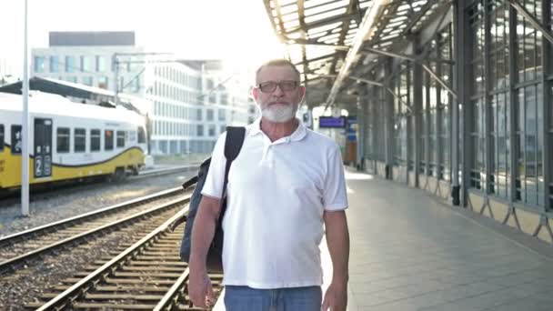 An elderly man with a backpack stands on the platform waiting for his train. — Stock Video