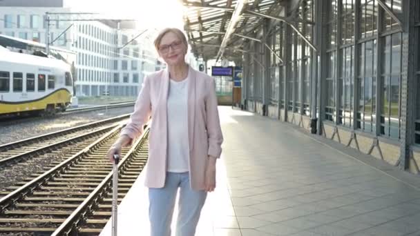 En äldre kvinna med resväska står på perrongen och väntar på tåget.. — Stockvideo