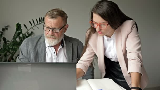 Két üzlettárs együtt dolgozik az irodában. Az idősebb férfi a munkájáról tárgyal fiatal kollégájával.. — Stock videók