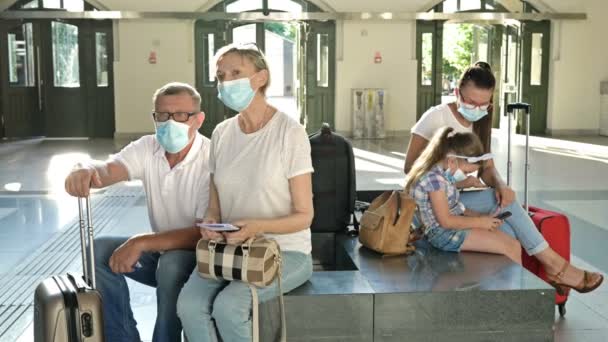 Ηλικιωμένο παντρεμένο ζευγάρι περιμένει την πτήση του στην αίθουσα αναμονής. Όλοι έχουν ιατρικές μάσκες στα πρόσωπά τους. Ταξίδι, τουρισμός κατά τη διάρκεια της επιδημίας coronavirus. — Αρχείο Βίντεο