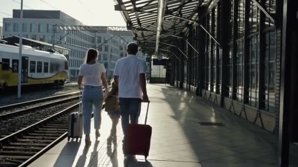 Família com uma menina de 5-6 anos de idade está andando ao longo da plataforma. Os passageiros estão a guardar malas. Visão traseira. — Vídeo de Stock