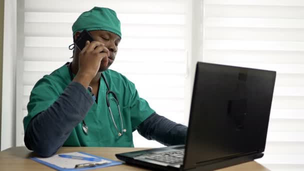 Mladý černý doktor nebo stážista mluví s někým po telefonu ve své kanceláři. — Stock video