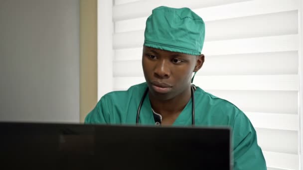 Jonge zwarte arts of stagiaire werkt aan een computer in zijn kantoor en is blij met iets. — Stockvideo