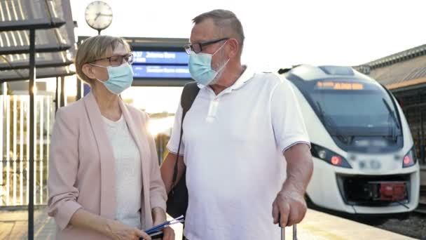 Un couple marié âgé portant un masque médical sur le visage se tient sur la plate-forme, attendant son train. Voyages, tourisme pendant l'épidémie COVID-19. — Video