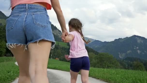 La giovane donna e la sua figlioletta corrono a piedi nudi lungo un sentiero sullo sfondo di una pittoresca zona montuosa. Vista posteriore. — Video Stock