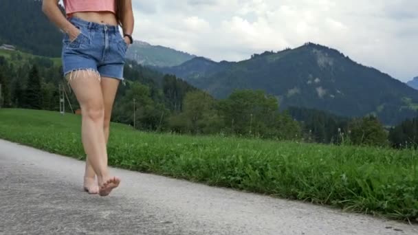 Giovane donna in pantaloncini e passeggiate a piedi nudi lungo un percorso sullo sfondo di una pittoresca zona montuosa e ammira il paesaggio. — Video Stock