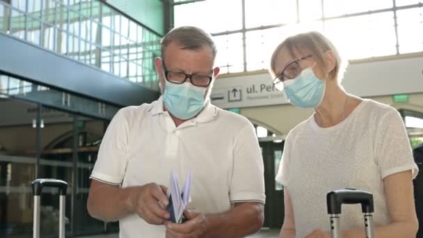 Ett äldre par väntar på flyget i väntrummet. Medicinska masker i deras ansikten. Resor, turism under coronavirus epidemin. — Stockvideo