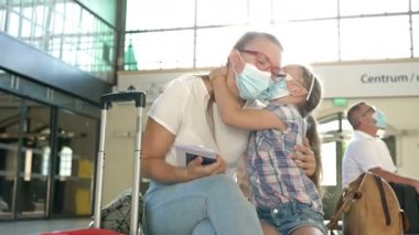 Küçük kızıyla birlikte genç bir kadın bekleme odasında uçmayı bekliyor. İkisinin de yüzünde tıbbi maske var. Çocuk annesini öpmek için maskesini çıkarıyor..