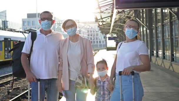 Familia de cuatro personas está esperando el tren en la estación. Todos los pasajeros usan máscaras médicas. Viajes, turismo durante la epidemia de COVID-19. — Vídeos de Stock