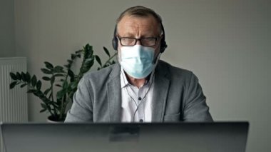 Coronavirüs salgını sırasında ofis işleri. Yaşlı işadamı dizüstü bilgisayar kullanıyor ve video görüşmesi yapıyor..