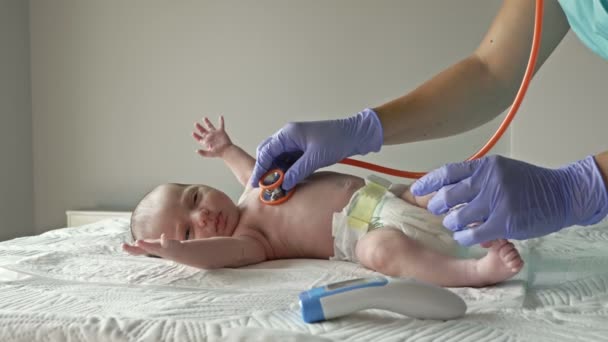 Неонатолог в латексных перчатках исследует новорожденного с помощью стетоскопа. — стоковое видео