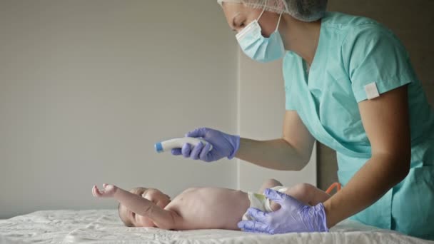 El pediatra mide la temperatura del recién nacido con un termómetro sin contacto en la clínica. Asistencia sanitaria. — Vídeos de Stock