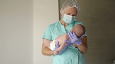 Pediyatrist kadın, yeni doğan bebeği kollarında tutuyor..