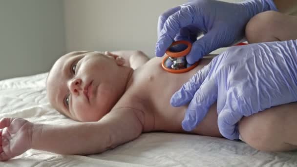 Неонатолог в латексных перчатках исследует новорожденного с помощью стетоскопа. Крупный план. — стоковое видео