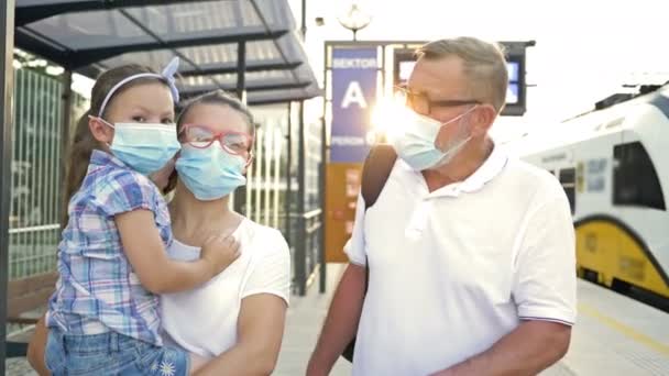 Dreiköpfige Familie mit Schutzmasken im Gesicht wartet am Bahnhof auf ihren Zug. — Stockvideo