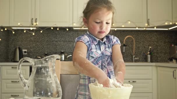Cute little girl jest ugniatanie ciasta na stole w kuchni. Nie jest w tym zbyt dobra.. — Wideo stockowe