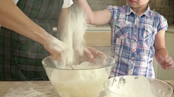 Een klein meisje helpt haar moeder in de keuken. Kind zeurt de bloem. Close-up. — Stockvideo