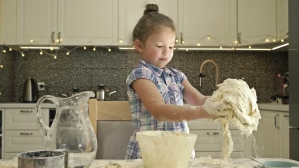 Cute little girl jest ugniatanie ciasta na stole w kuchni. Nie jest w tym zbyt dobra.. — Wideo stockowe