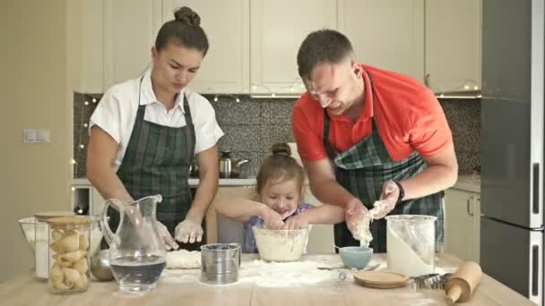 Веселая супружеская пара с маленькой дочерью, готовят тесто вместе, наслаждаются семейными мероприятиями. — стоковое видео