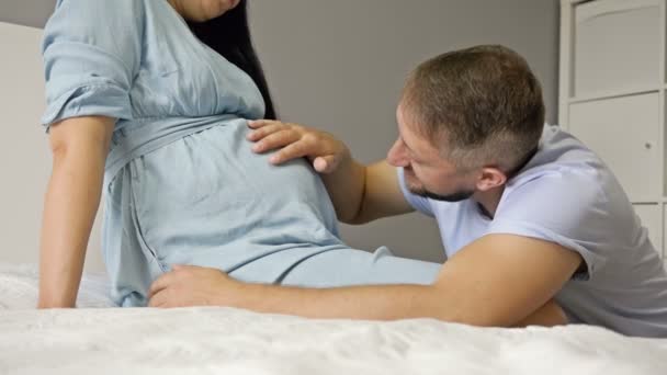 Homem feliz acariciando e beijando a barriga de sua esposa grávida. Esperando o nascimento de uma criança. — Vídeo de Stock