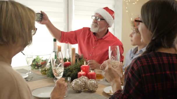 Традиційна святкова різдвяна вечеря в родині. Дідусь у Санта - капелюсі робить селфі зі своєю сім "єю.. — стокове відео