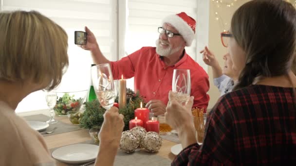 Traditioneel kerstdiner in de familie. opa draagt een kerstmuts neemt een selfie met zijn familie. — Stockvideo
