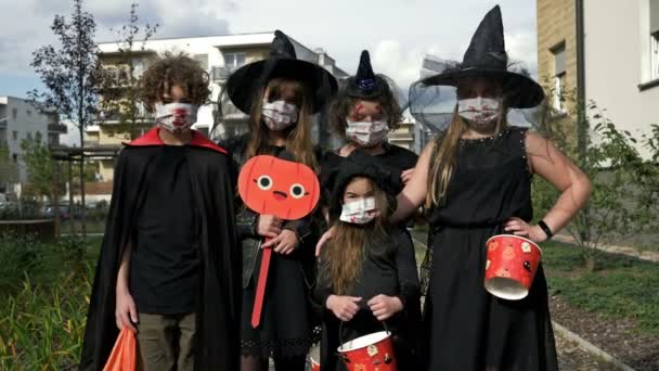 Retrato de grupo de niños en traje de fantasía negro. Todos tienen máscaras médicas en la cara. Halloween durante la pandemia del covid19 coronavirus. — Vídeo de stock