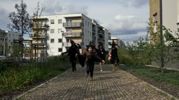 Siyah süslü elbiseli beş çocuklu bir grup caddede koşuyor. Herkesin yüzünde coşkulu bir gülümseme vardır. Çocuklar Cadılar Bayramı 'nı sever. — Stok video