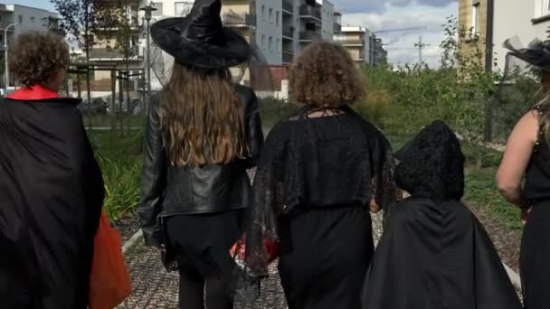 Vijf kinderen van verschillende leeftijden in zwarte maskerade kostuums gaan van huis naar huis om te bedelen voor snoep. Kinderen houden van Halloween. Achteraanzicht. — Stockvideo