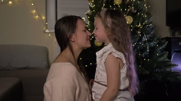 Молодая женщина и ее маленькая дочь нежно обнимают друг друга на фоне рождественской елки. — стоковое видео