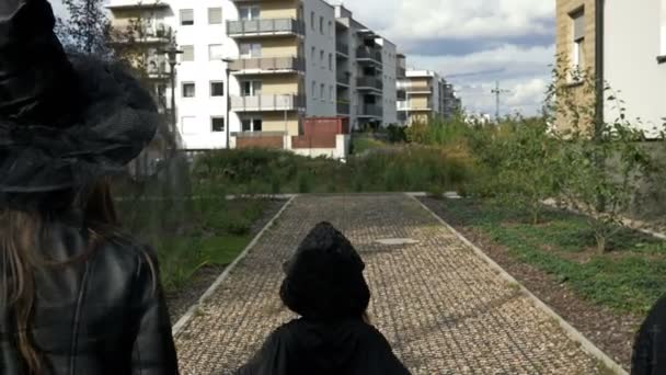 Cinque bambini di diverse età in costumi mascherati neri vanno di casa in casa a mendicare dolci. I bambini amano Halloween. Vista posteriore. — Video Stock