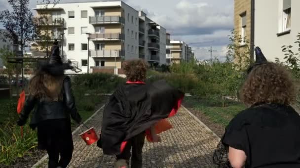 Un grupo de niños con disfraces de máscaras negras están corriendo por la calle. Halloween. Vista trasera. — Vídeo de stock