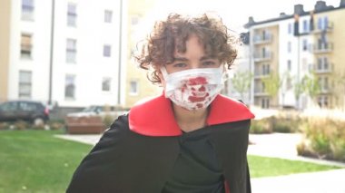 Vampir kostümü giymiş ve yüzünde koruyucu bir maskeyle genç bir çocuğun portresi. Koronavirüs salgını sırasında Cadılar Bayramı.