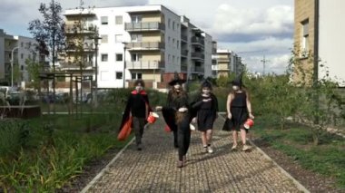 Bir grup siyah maskeli çocuk caddede yürüyorlar. Herkesin yüzünde tıbbi maske vardır. Covid19 Coronavirus salgını sırasında Cadılar Bayramı.