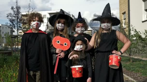 Retrato de grupo de niños en traje de fantasía negro. Todos tienen máscaras médicas en la cara. Halloween durante la pandemia del covid19 coronavirus. — Vídeo de stock