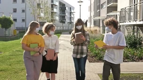 Vier jugendliche Schulkinder in medizinischen Masken und mit Büchern in der Hand. Akademisches Jahr inmitten der Coronavirus-Pandemie. Zurück zur Schule. — Stockvideo