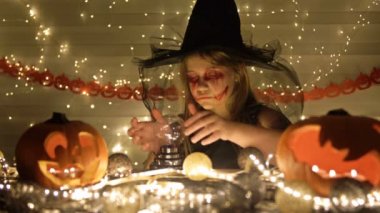 Cadı gibi giyinmiş, yüzünde korkunç bir makyajla genç bir kız. Kız sihirli bir topu çağırır. Koyu altın arka plan. Cadılar Bayramı.