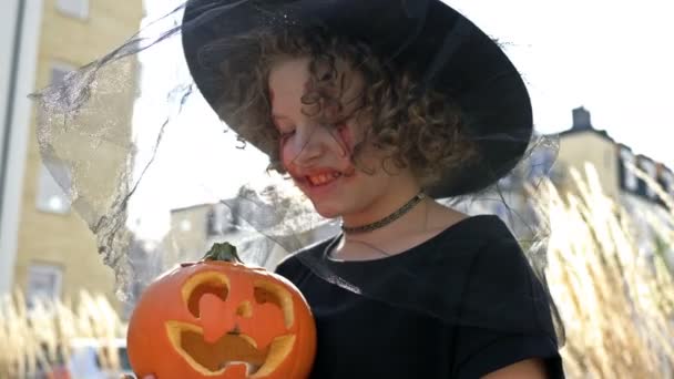 Portret van een tienermeisje verkleed als heks met enge make-up op haar gezicht en met een pompoen. Halloween. — Stockvideo