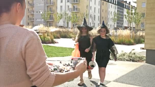 女性は顔に怖いメイクで黒空想のドレスでお菓子2人の女の子を扱います.ハロウィンの伝統. — ストック動画