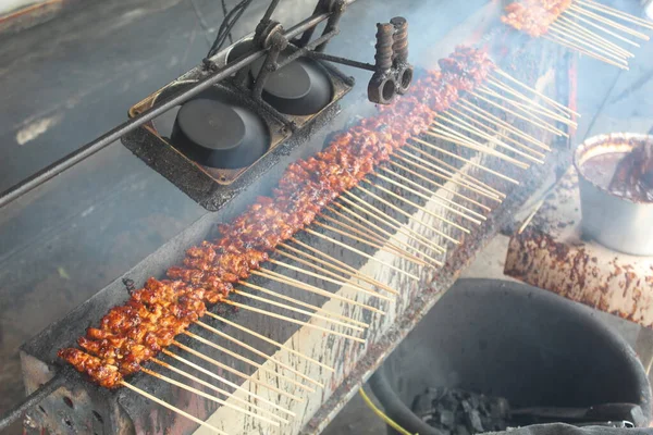 Satay with goat meat prepared on a charcoal grill. Smoke billows from the grill.
